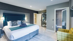 Une chambre d’hôtel moderne avec un grand lit, une table de chevet, une commode et un dressing.