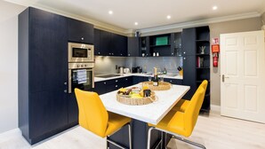 Une cuisine moderne avec des meubles de couleur sombre, des appareils en acier inoxydable, un plan de travail en marbre et des chaises jaunes.