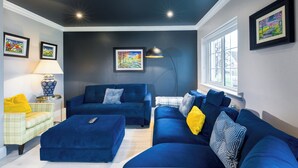 Un salon moderne avec un mur d’accent de couleur foncée, un canapé bleu, un fauteuil jaune et une lampe.