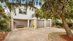 Une maison moderne à deux étages, dotée d’un garage fermé, d’un banc et d’un arbre dans le jardin.