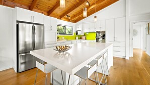 A modern kitchen with white cabinetry, stainless steel appliances, and a large island with bar stools. - Sandy Feet Retreat in Cape Woolamai (Cape Woolamai)