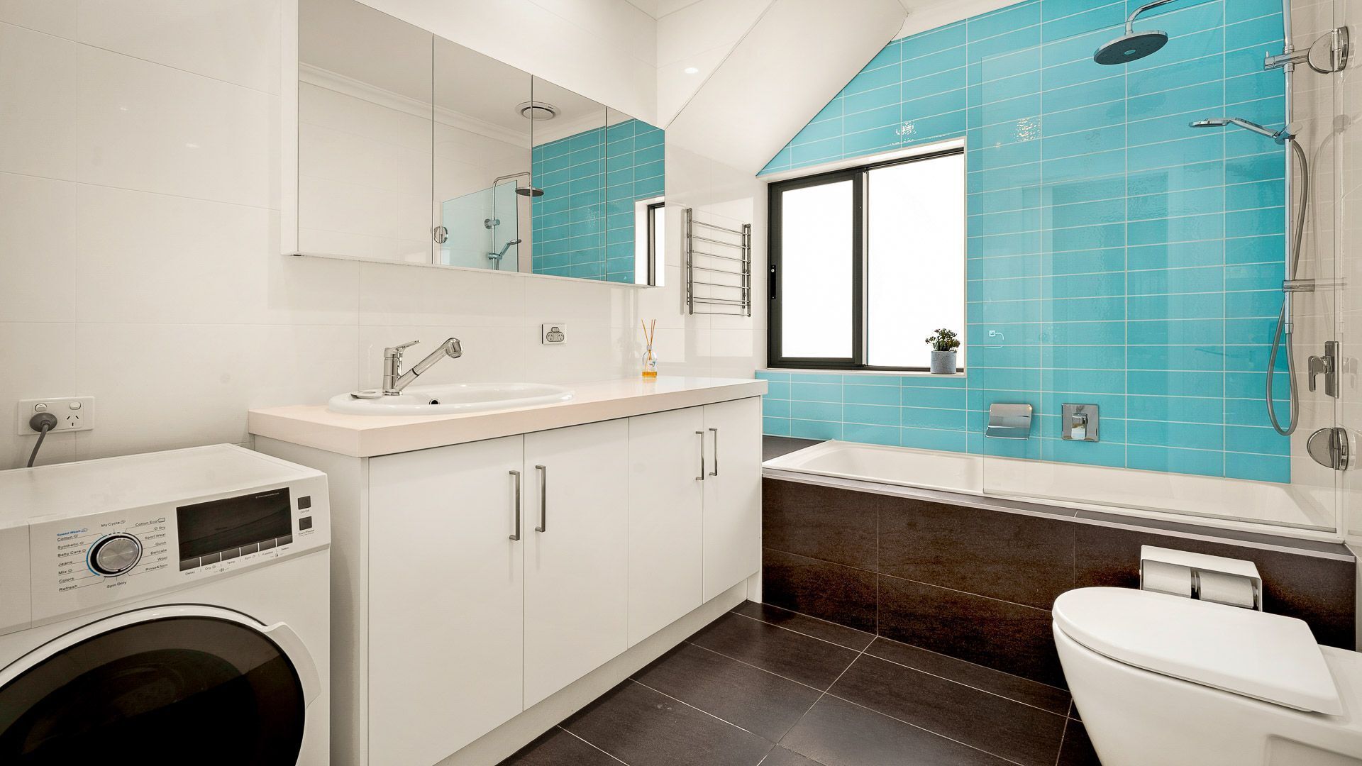 A modern bathroom with a washing machine, a sink, and a toilet.