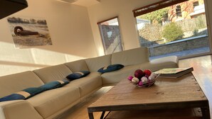 A modern living room with a beige sectional sofa, a wooden coffee table with a decorative bowl, and large windows offering a view of the outside. - L'Arabesque, charming villa with private pool (Arradon)