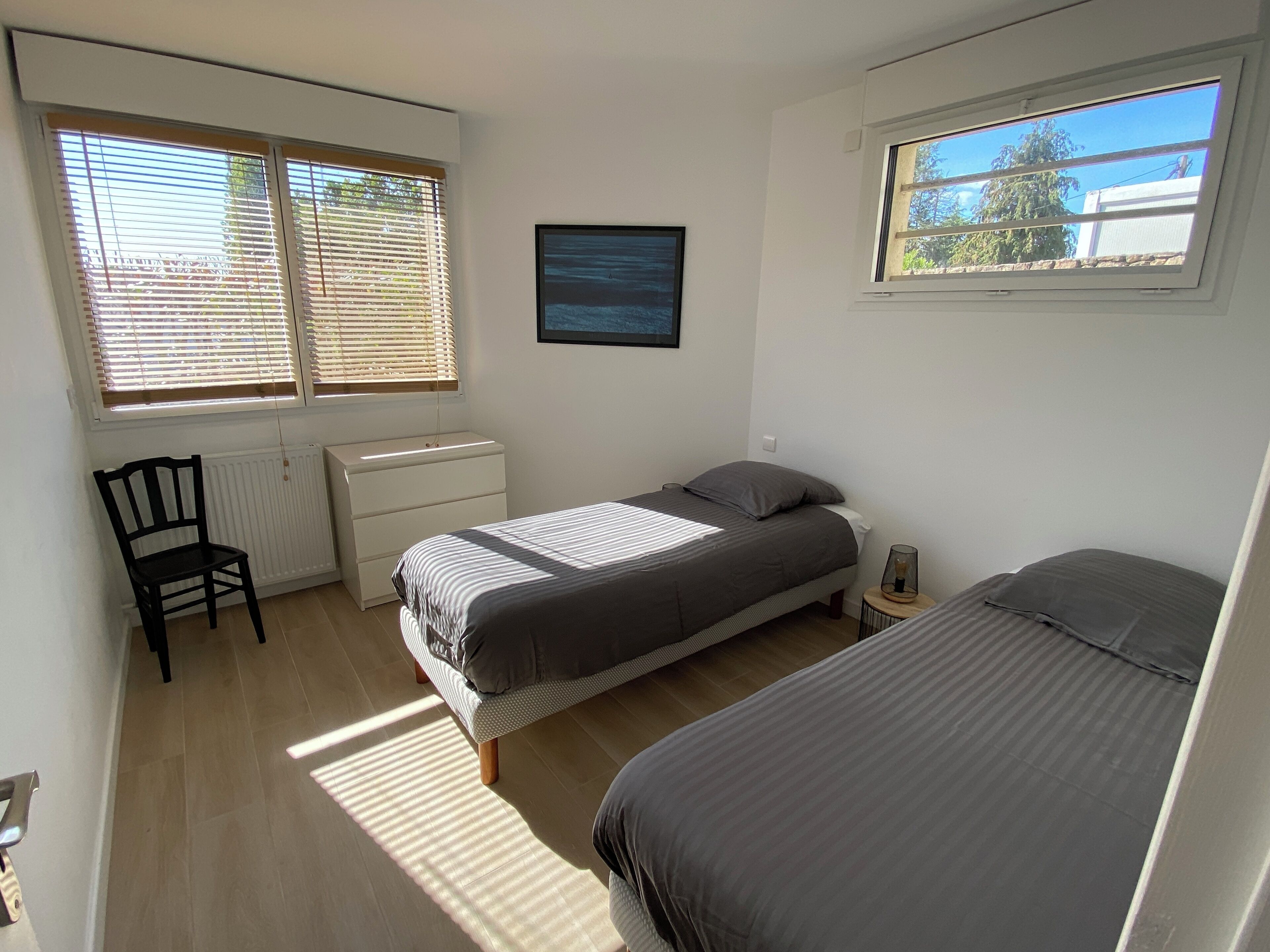 Ein Schlafzimmer mit zwei Betten, einem Sessel, einem Schminktisch und zwei Fenstern mit Jalousien.