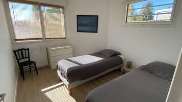 Ein Schlafzimmer mit zwei Betten, einem Sessel, einem Schminktisch und zwei Fenstern mit Jalousien.