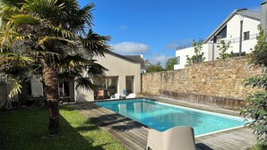 A swimming pool with a wooden deck, lounge chairs, and a stone wall. - L'Arabesque, charming villa with private pool (Arradon)