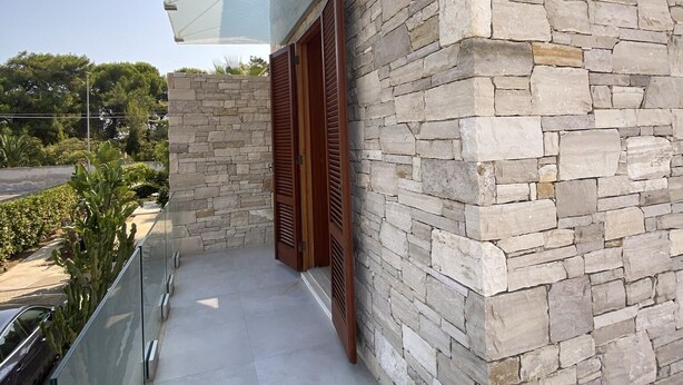 Ein mit Naturstein verkleidetes Gebäude mit einem Glasbalkon und Holzläden.