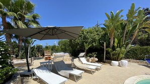 Ein Poolbereich mit Liegestühlen, einem großen Sonnenschirm und einem Whirlpool.