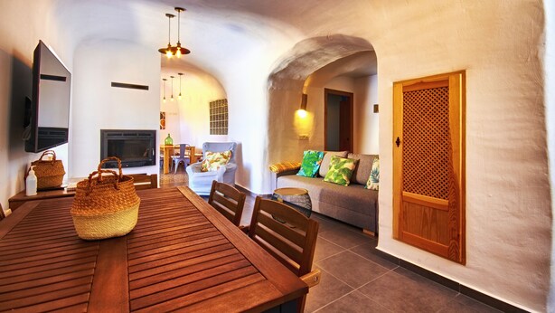 A dining area with a wooden table and chairs, a woven basket, and a sofa with cushions.