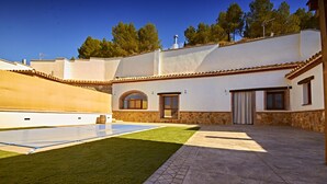 A spacious patio with a swimming pool, stone walls, and a view of the surrounding landscape.