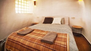 A bedroom with a bed, two pillows, a blanket, a bedside table, a lamp, and a window.