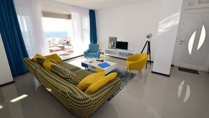 Ein modernes Wohnzimmer mit einem gemusterten Sofa, gelben Kissen, einem blauen Sessel und einer weißen Unterhaltungsecke.