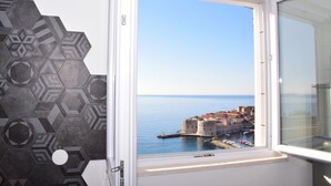 Ein Zimmer mit Fenster und Blick auf eine Küstenstadt, einer Wand mit geometrischem Muster und einer weißen Tür.