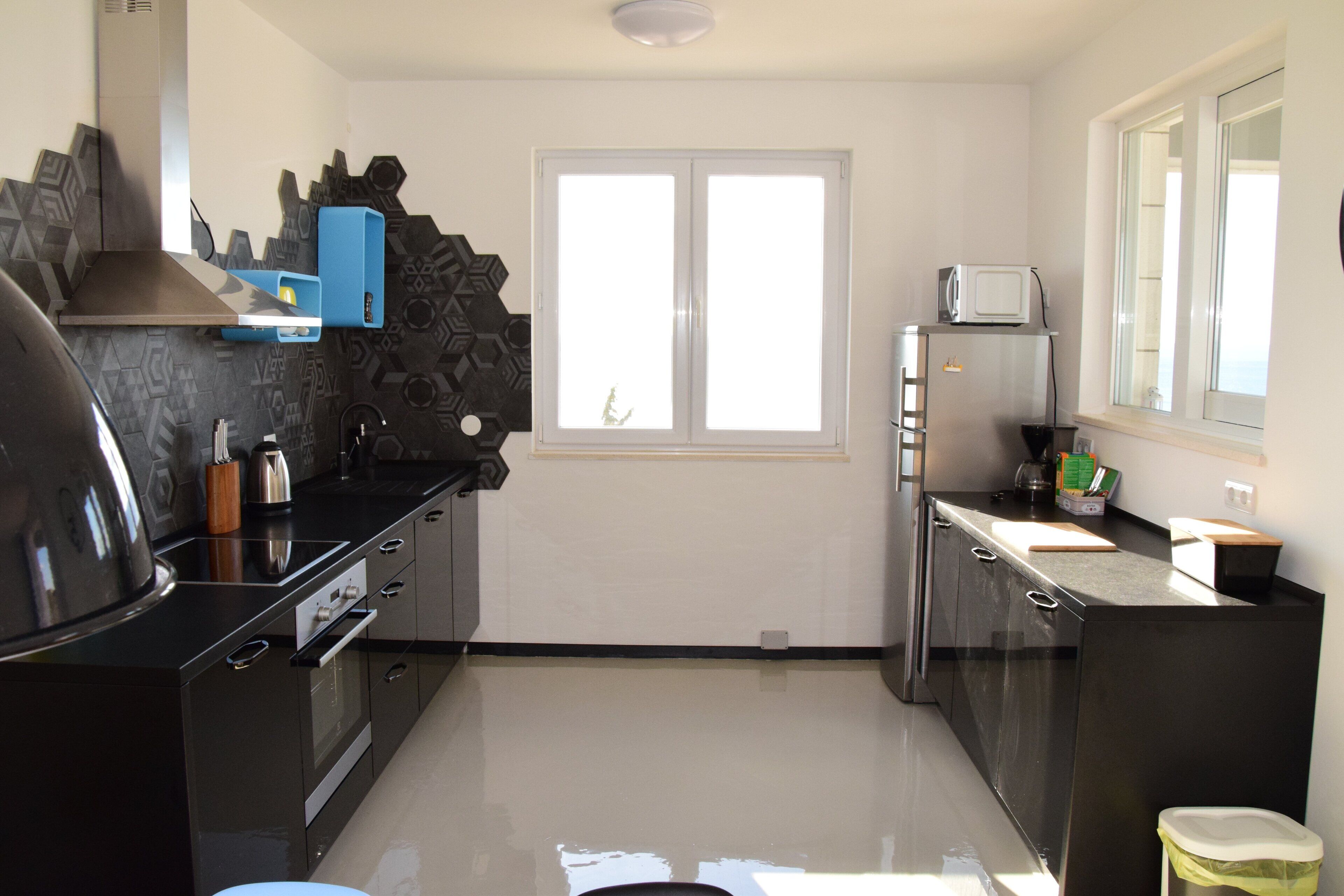Una cocina moderna con armarios negros, una campana extractora de acero inoxidable y un ventanal sobre el fregadero.