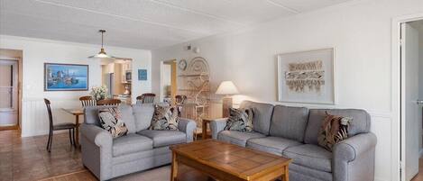 Ein Wohnzimmer mit zwei grauen Sofas, einem Holztisch und einem Essbereich mit Tisch und Stühlen.