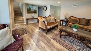 Un salon spacieux avec un escalier en bois, un grand tableau, une horloge et deux canapés.