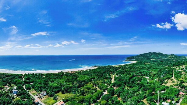 A coastal landscape with a beach, dense greenery, and a clear sky. - 7 min walk to Surfing Paradise, Pool & Ocean Fun (Playa Grande)