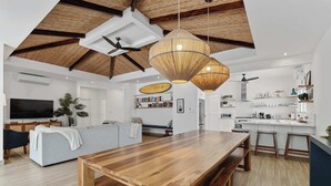 A spacious living area with a wooden dining table, a sofa, and a kitchen in the background. - 7 min walk to Surfing Paradise, Pool & Ocean Fun (Playa Grande)