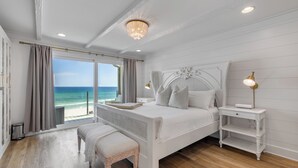 Un dormitorio con una cama grande, un banco, una mesita de noche y vista al océano.