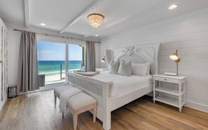 Une chambre avec un grand lit, un banc, une table de chevet et une vue sur l’océan.