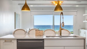 A kitchen with a view of the ocean, two pendant lights, and a sink with a faucet.