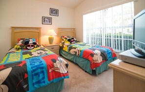 A hotel room with two beds, each with Mickey Mouse themed bedding. There is a window with blinds, a lamp on each nightstand, and a television on a stand. - Cumbrian Retreat 4 Bedroom Home by RedAwning (Kissimmee)
