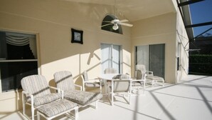 Eine sonnendurchflutete Terrasse mit weißer Möbel, darunter Stühle und ein Tisch, sowie einem Deckenventilator.