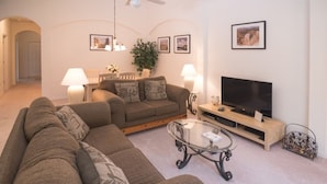 Ein Wohnzimmer mit Ecksofa, Glastisch, Flachbildfernseher und einer Lampe.
