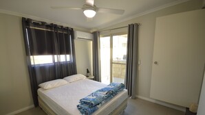 Une chambre avec un lit, un ventilateur de plafond et une vue sur l’extérieur.