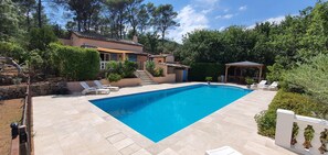 Ein rechteckiger Swimmingpool mit Fliesen umrandet, umgeben von einer Steinmauer und üppiger Bepflanzung.