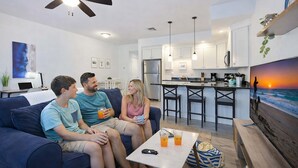 A modern living room with a sofa, a coffee table, and a TV displaying a sunset scene.