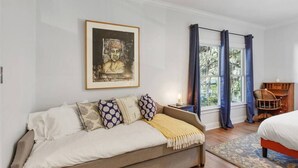A bedroom with a sofa bed, a framed artwork on the wall, a window with curtains, and a chair by the window. - Starland Town House, Walk to the Park, 2 Parking Spaces (Savannah)