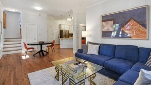 A modern living room with a blue sofa, a glass coffee table, and a dining area with a black table and red chairs. - Starland Town House, Walk to the Park, 2 Parking Spaces (Savannah)