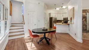 A modern kitchen with white cabinets, a central island, and a dining area with a round table and red chairs. - Starland Town House, Walk to the Park, 2 Parking Spaces (Savannah)