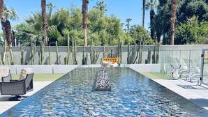 A pool with clear water, surrounded by palm trees and cacti, with lounge chairs and a sunbed in the background. - Palm Desert Velo - Modern Condo w Spa (Palm Desert)
