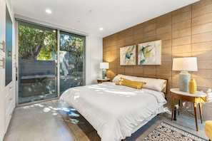 Quarto moderno com uma cama grande, porta de vidro deslizante para área externa e obra de arte na parede.