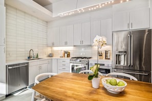 A modern kitchen with white cabinetry, stainless steel appliances, a wooden dining table, and a potted orchid.