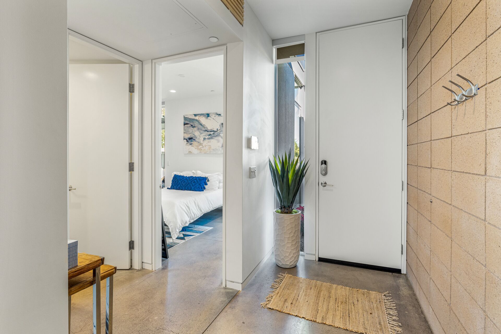 A hallway with a bed, a potted plant, and a textured rug.