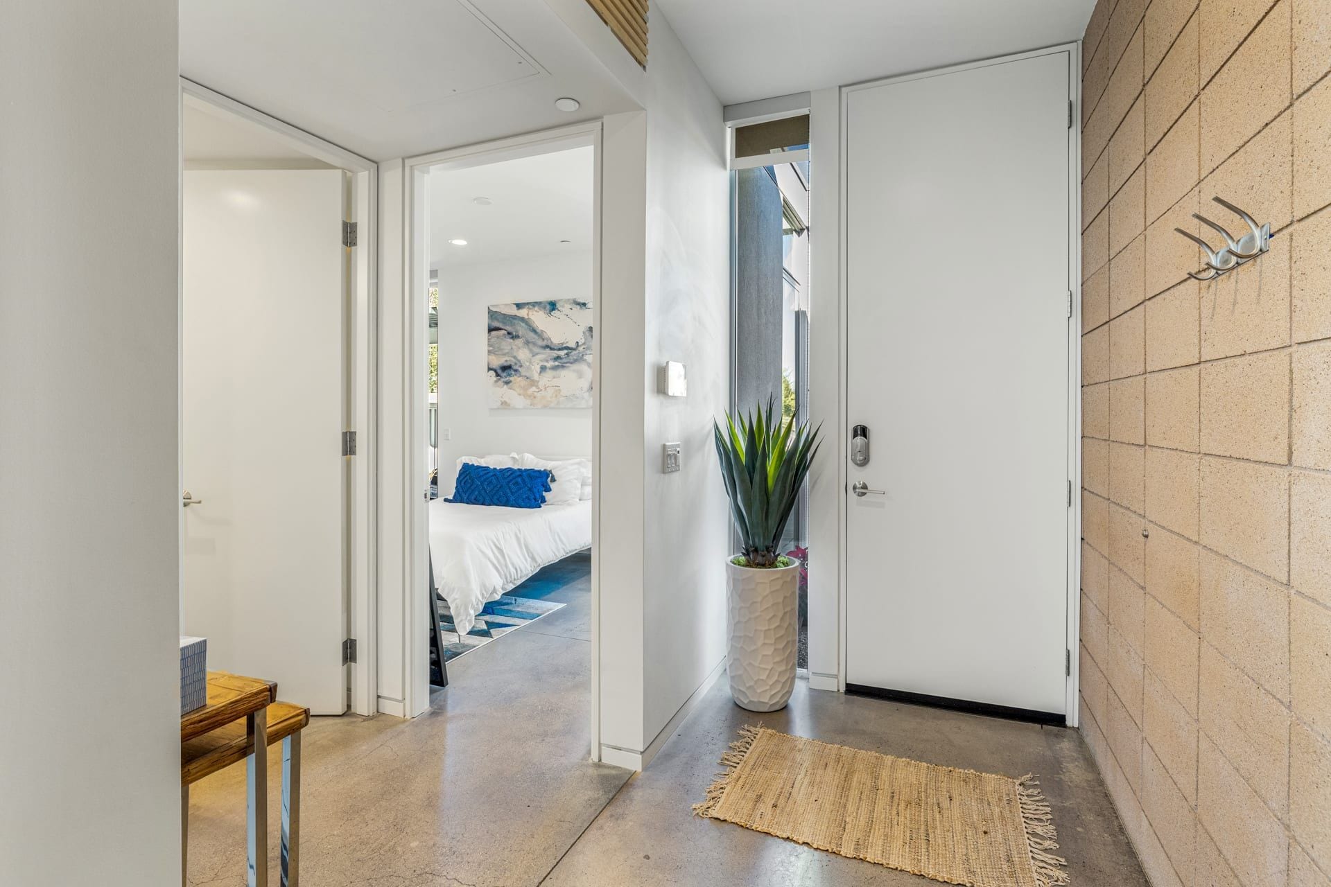 A hallway leading to a bedroom with a bed, a potted plant, and a textured rug.