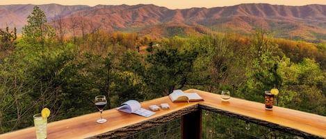 Una barra de madera con vistas a montañas, un libro, vasos y una bebida.