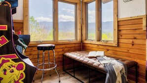 Una habitación tipo cabaña con un banco, un taburete y vistas a las montañas a través de amplias ventanas.