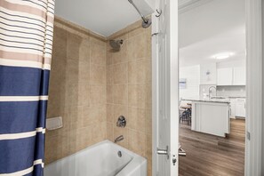 Une salle de bain équipée d’une baignoire, d’une douche et d’une porte donnant sur un espace cuisine.