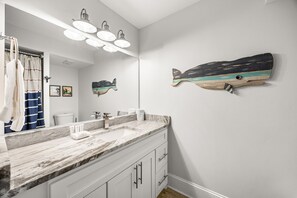 Une salle de bain avec un comptoir en marbre, un grand miroir et une décoration murale représentant des poissons.