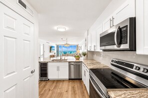 A modern kitchen with white cabinetry, stainless steel appliances, and a view to the outside. - Gulfside 505 - Gulf Front, Community Pool, Hot Tub, Tennis, Basketball, Fitness! (Miramar Beach)