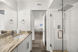 Une salle de bain moderne avec un comptoir en marbre, une douche en verre et un couloir menant à une salle à manger.