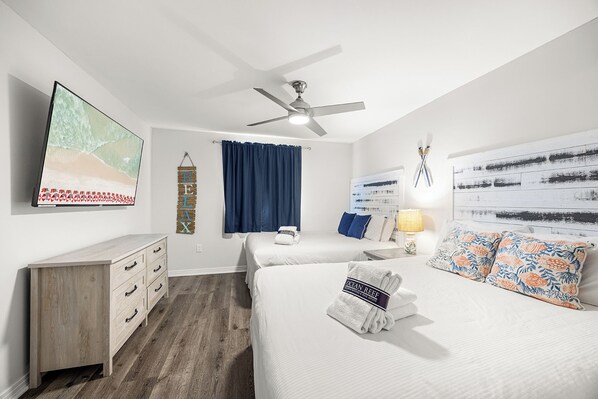 Une chambre d’hôtel comprenant un lit, un bureau, un ventilateur de plafond, un téléviseur fixé au mur et un élément décoratif mural.