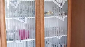 Ein Holzkabinett mit Glastüren, das Geschirr und Küchenutensilien beherbergt.