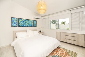 A bedroom with a bed, a window with shutters, and two wall-mounted artworks.