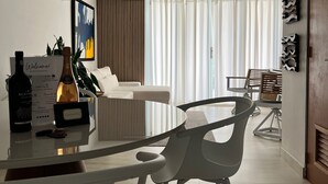A modern living room with a sofa, a glass coffee table, and a dining area with chairs. - Dream Villa · Direct Beach Access · Pool · 2BR Gated · Dorado, PR (Dorado)