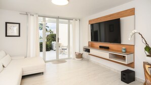 A modern living room with a sofa, TV, and a sliding glass door leading to an outdoor area. - Dream Villa · Direct Beach Access · Pool · 2BR Gated · Dorado, PR (Dorado)